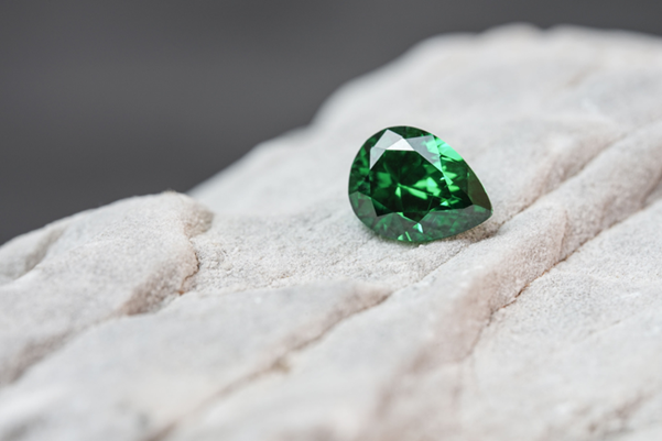 A close-up of a brilliant green, pear-shaped authentic gemstone