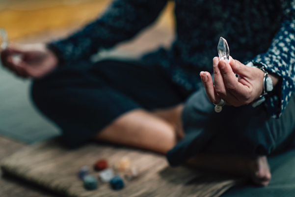 A person in a meditative pose holding a clear quartz crystal