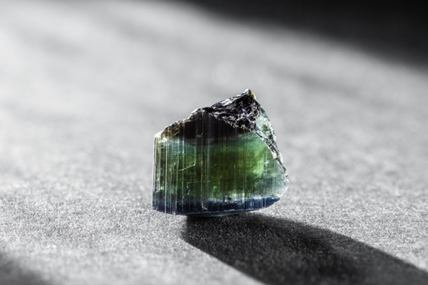 A rough, uncut tourmaline crystal displaying a range of colors from dark green to blue