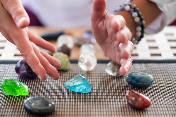 Hands sorting through a table filled with various colorful tumbled stones and crystal spheres, representing the wide selection and fair prices offered by wholesalers.