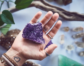 A person holding a raw, purple amethyst crystal cluster