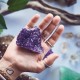 A person holding a raw, purple amethyst crystal cluster