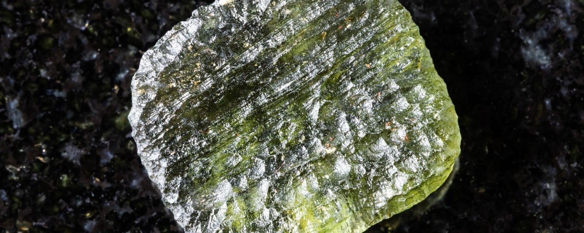 Rough moldavite tektite formed by meteorite impact, displayed on a black background