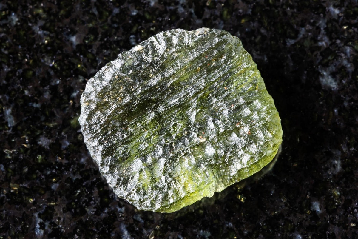 Rough moldavite tektite formed by meteorite impact, displayed on a black background