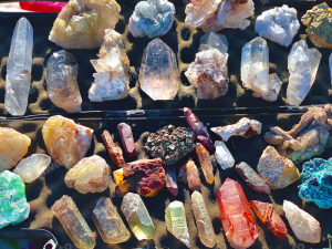 Overhead view of a wide assortment of natural rough crystals and gemstones in various colours and formations laid out on a flat surface, representing the range of stock evaluated in bulk wholesale crystal orders
