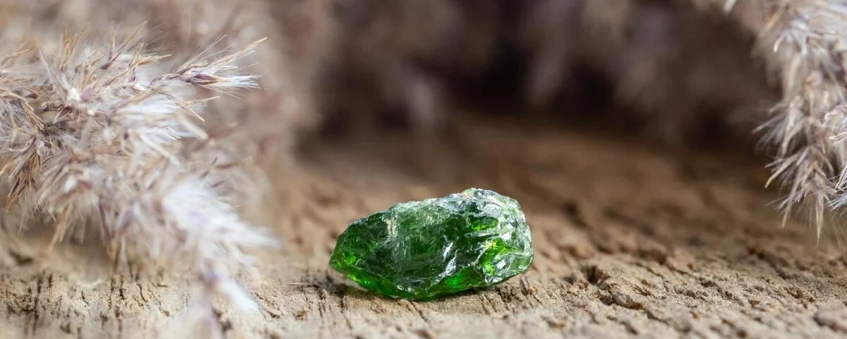 Small raw moldavite stone with rough green surface resting on sandy ground outdoors