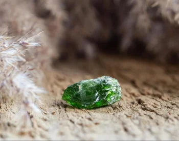 Small raw moldavite stone with rough green surface resting on sandy ground outdoors