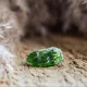 Small raw moldavite stone with rough green surface resting on sandy ground outdoors