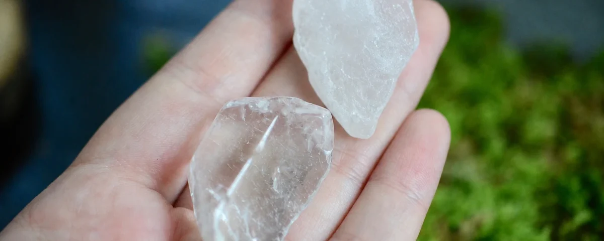 Two clear quartz tumbled stones held in an open palm over moss