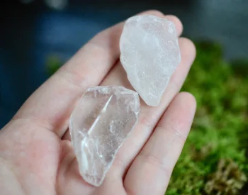 Two clear quartz tumbled stones held in an open palm over moss