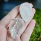 Two clear quartz tumbled stones held in an open palm over moss