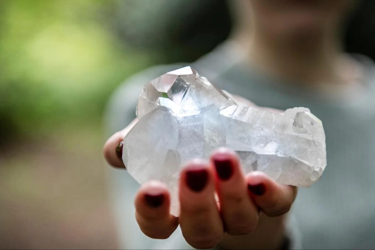 Person holding a large clear quartz cluster outdoors
